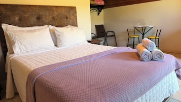 A bed with a headboard, a table with chairs, and a small table with a glass.