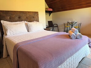 A bed with a headboard, a table with chairs, and a small table with a glass.