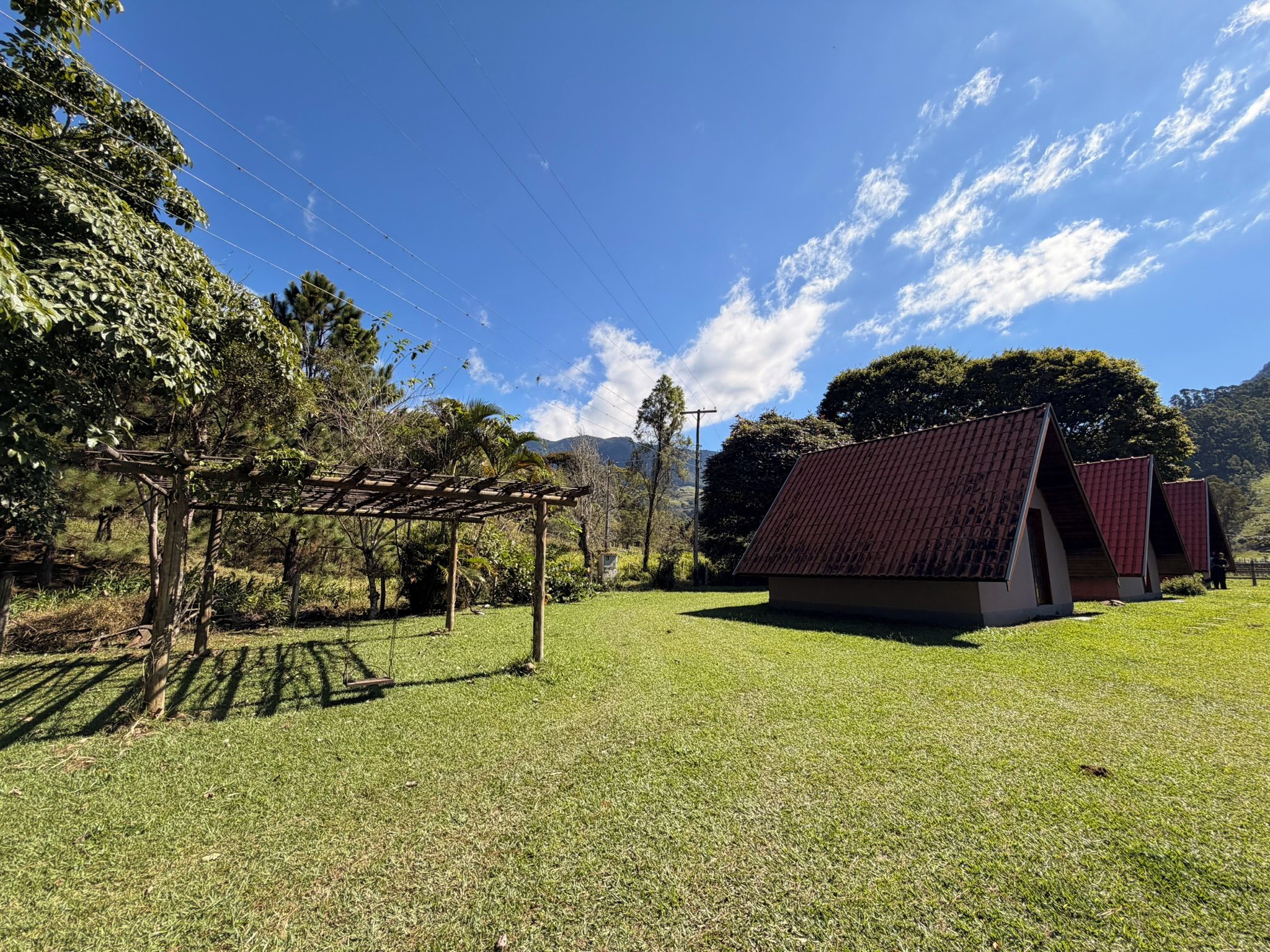 Uma área gramada com uma pérgula de madeira e um pequeno edifício com telhado vermelho.