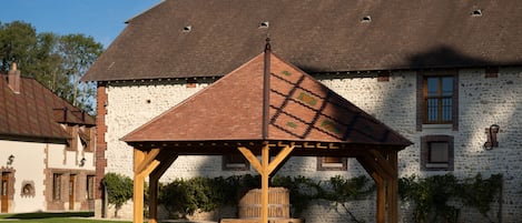 Un kiosque en bois, doté d’un toit en pente, se trouve devant un bâtiment blanc à la façade en briques.