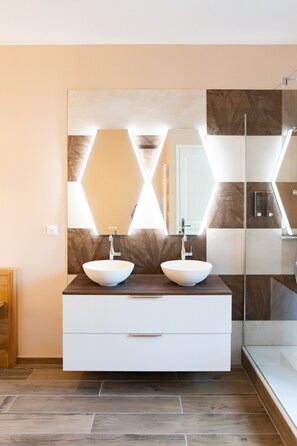 Ein modernes Badezimmer mit zwei Waschbecken, einem großen Spiegel und einer Duschkabine aus Glas.