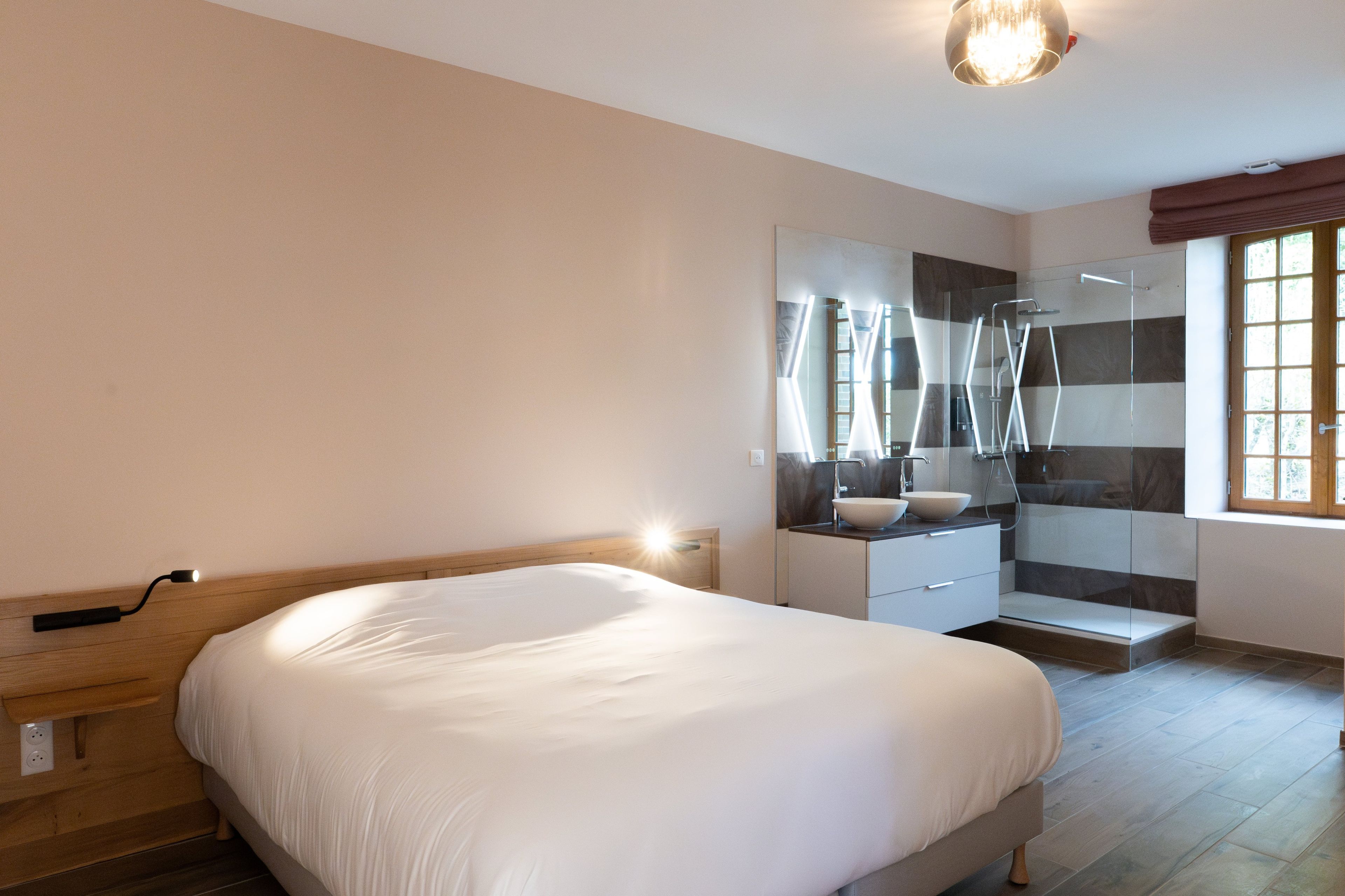 A modern bedroom with a large bed, a bathroom with a glass shower, and a window with curtains.