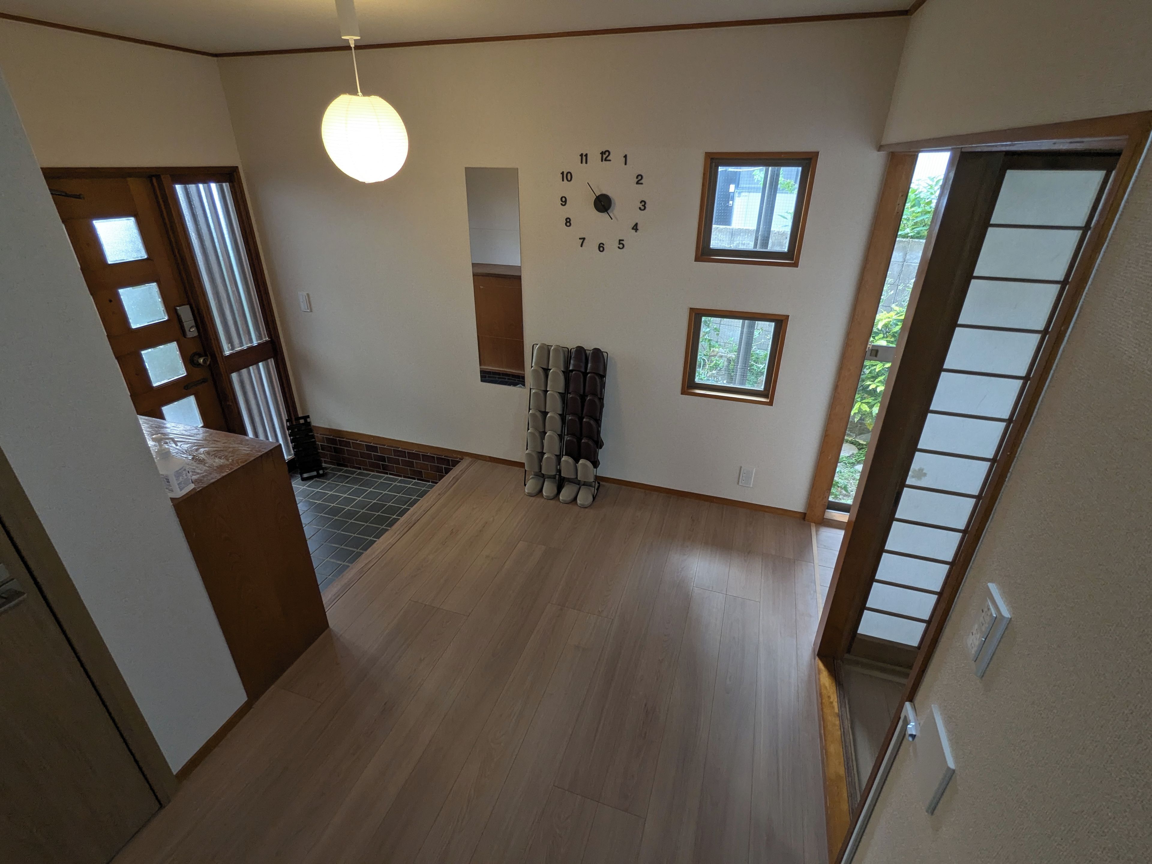 A room with a wooden floor, a clock on the wall, and a window.