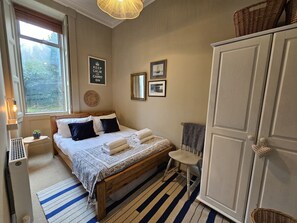 Une chambre à coucher comprenant un lit, une table de chevet, une chaise, une armoire et une fenêtre.