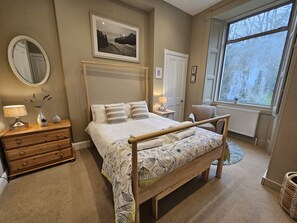 Ein Schlafzimmer mit einem Bett, Nachttischen, einer Kommode, einem Fenster und einem gerahmten Bild an der Wand.