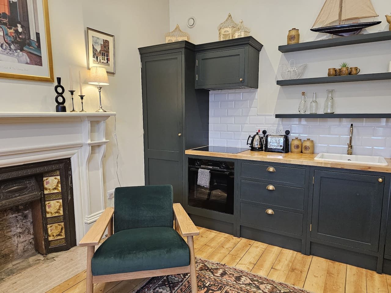 Une cuisine avec des meubles de couleur sombre, un plan de travail en bois et une chaise verte.
