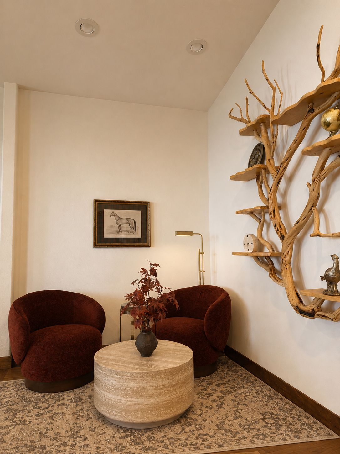 A living room with two armchairs, a round coffee table with a vase, a wall-mounted shelf with decorative items, and a framed picture on the wall.