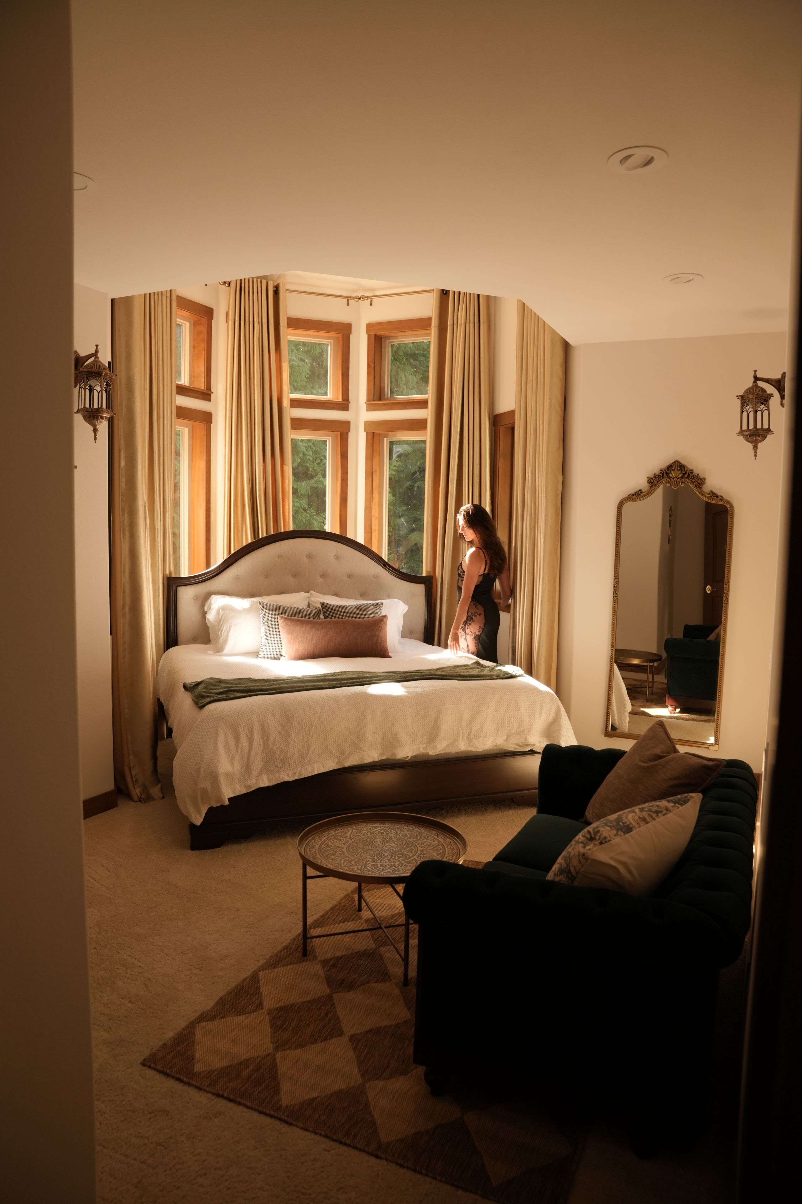 A bedroom with a bed, a nightstand, a chair, a mirror, and a window with curtains.