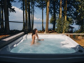 Ein Whirlpool mit einer Person darin, umgeben von Bäumen und Blick auf das Wasser.