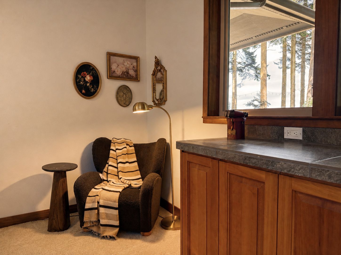 A cozy corner with a chair, a lamp, and a window with a view of trees.
