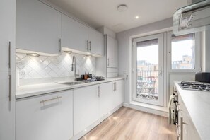 Eine moderne Küche mit weißen Schränken, einer Fischgrät-Spritzwand, einem Gasherd und einem Fenster mit Blick auf Gebäude.
