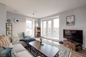 A modern living room with a sofa, coffee table, and a television. There is a bookshelf and a window with a view of buildings. - Central Edinburgh 2 Bed Apt near Royal Mile (Edinburgh)