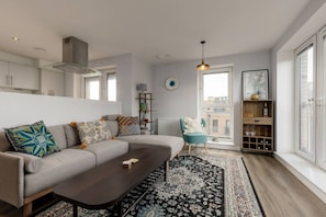 Een moderne woonkamer met een bank, salontafel en uitzicht op de stad door grote ramen.