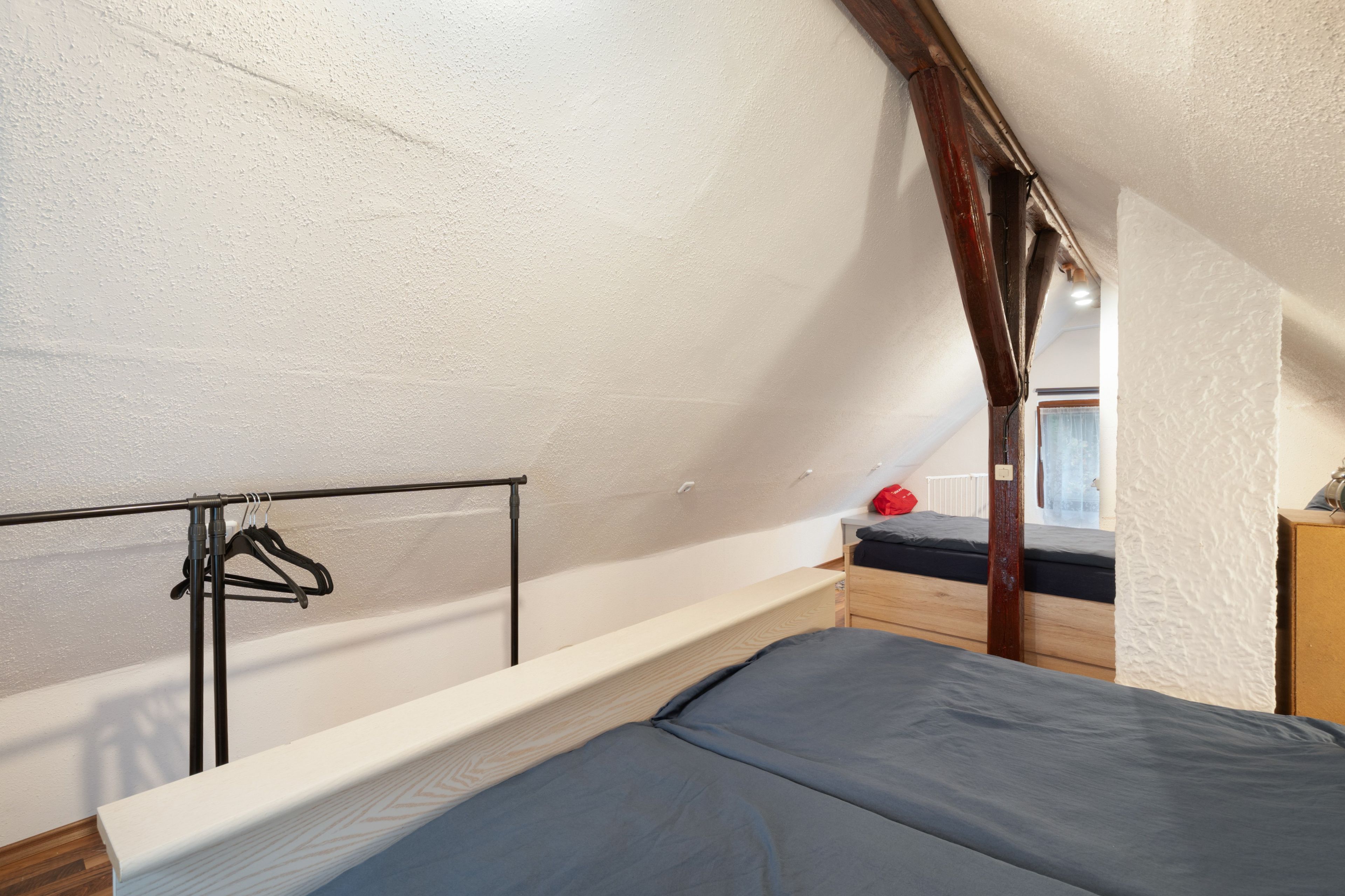 A dormitory-style room with a bunk bed, a wooden wardrobe, and a metal rack with hangers.