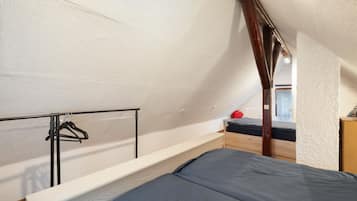 A dormitory-style room with a bunk bed, a wooden wardrobe, and a metal rack with hangers.