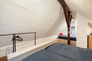 A dormitory-style room with a bunk bed, a wooden wardrobe, and a metal rack with hangers.