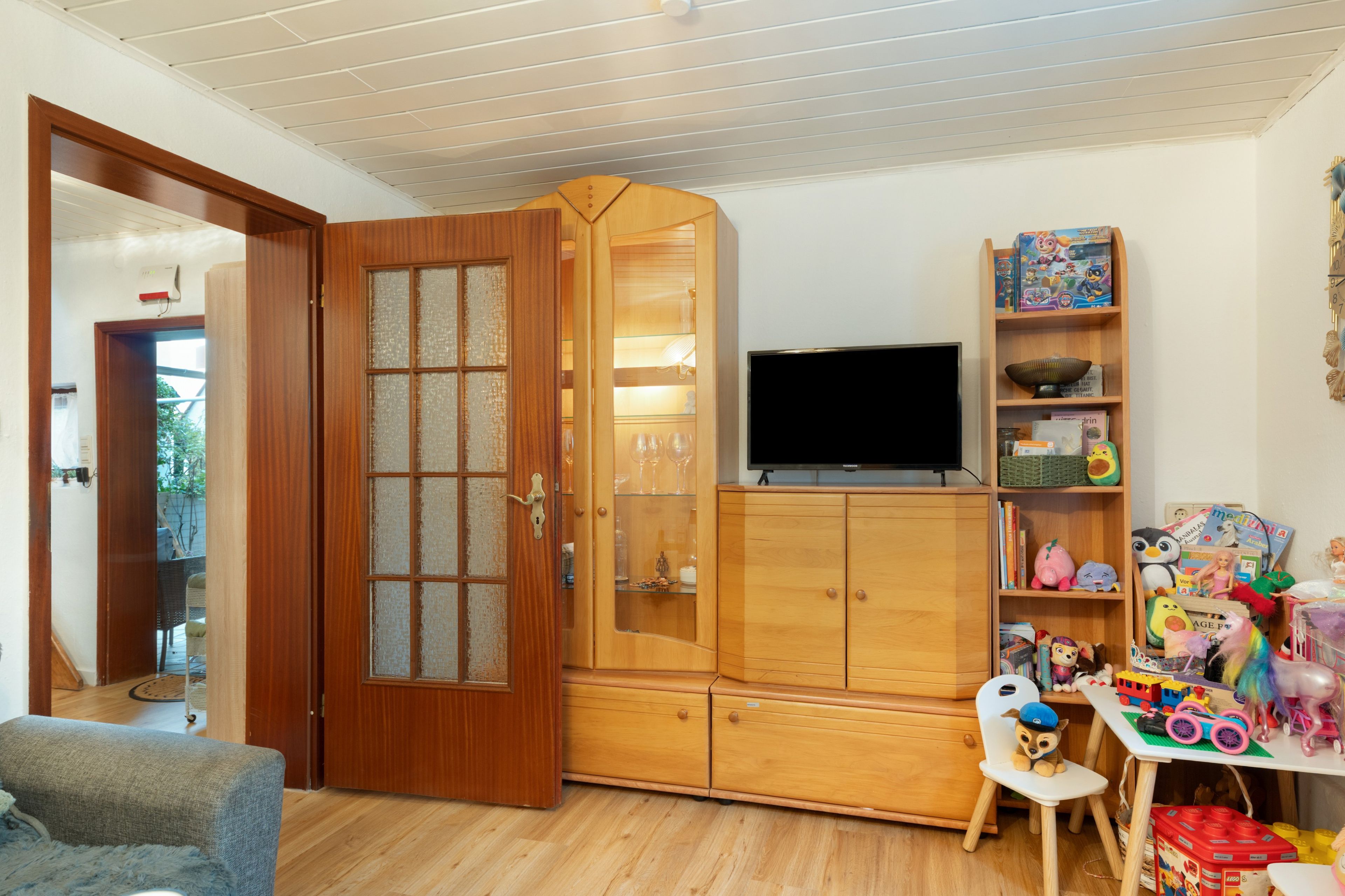 A room with a wooden cabinet, a television, and a bookshelf with children's toys.