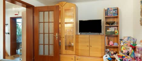 A room with a wooden cabinet, a television, and a bookshelf with children's toys.