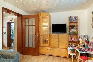 A room with a wooden cabinet, a television, and a bookshelf with children's toys.