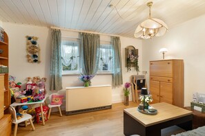 A well-lit room with a wooden ceiling, a radiator, a desk with toys, a chair, and a table with a lamp.