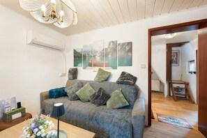 Ein Wohnzimmer mit einer Couch, einer Lampe, einer Vase mit Blumen und einer Wand-Klimaanlage.