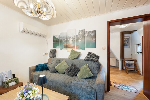 A living room with a sofa, a lamp, a vase with flowers, and a wall-mounted air conditioner.