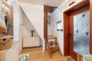 A narrow hallway with a wooden door, a radiator, a small table with a vase, and a welcome mat.
