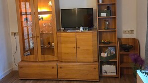 Een houten kast met een televisie erop, een klein plankje met spullen, en een houten vloer.