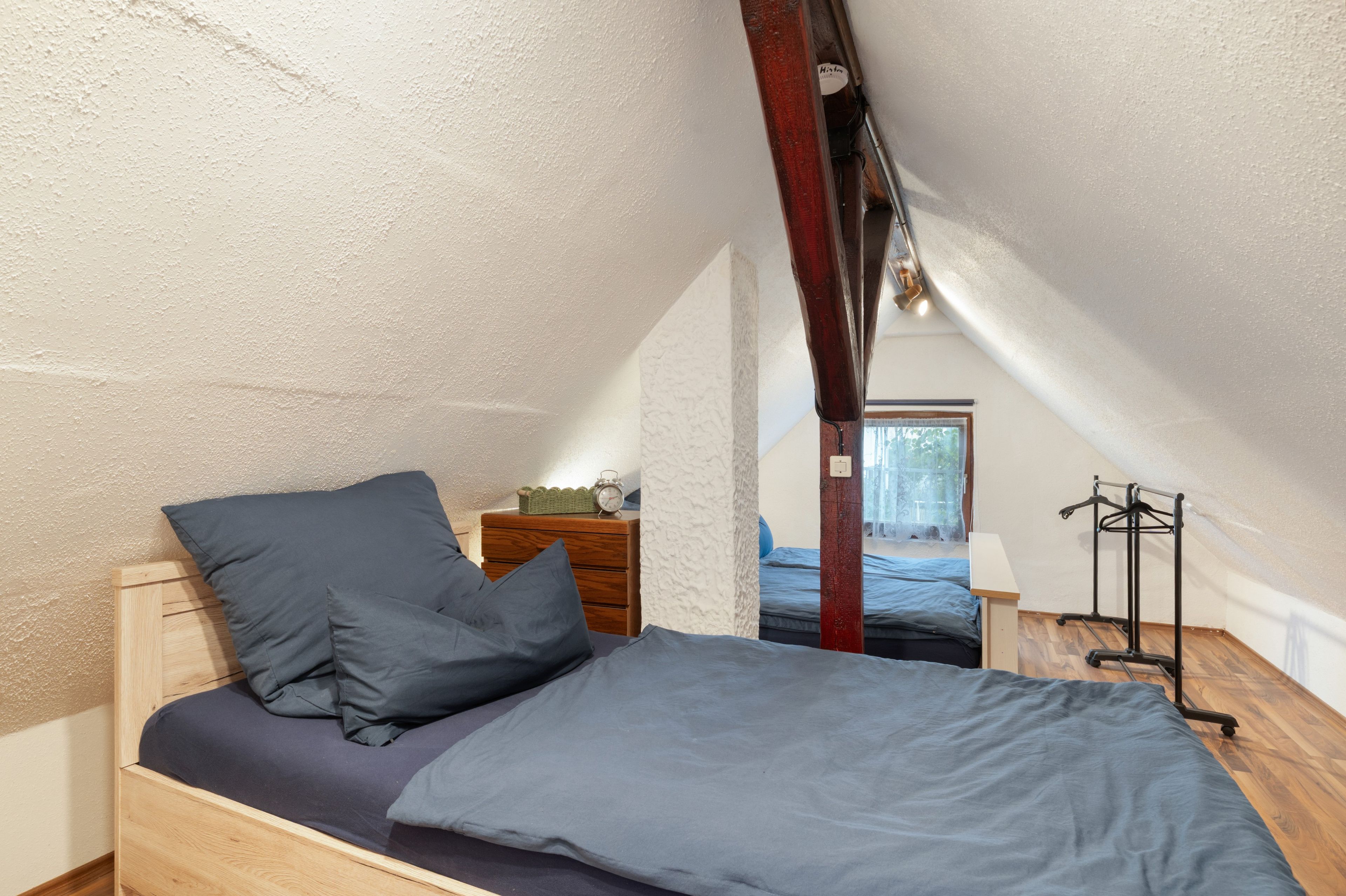 Un dormitorio acogedor en el ático, con una cama individual, un aparador de madera y un perchero.
