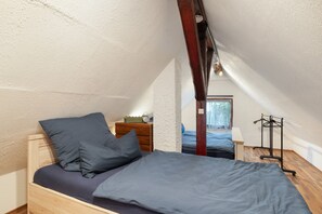 A small, cozy attic bedroom with a single bed, a wooden dresser, and a hanging coat rack.