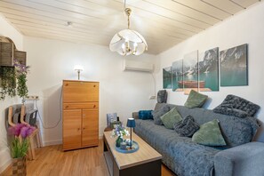 Un salon chaleureux avec un meuble en bois, un canapé agrémenté de coussins, une table sur laquelle est posé un vase de fleurs et des œuvres d’art accrochées au mur.