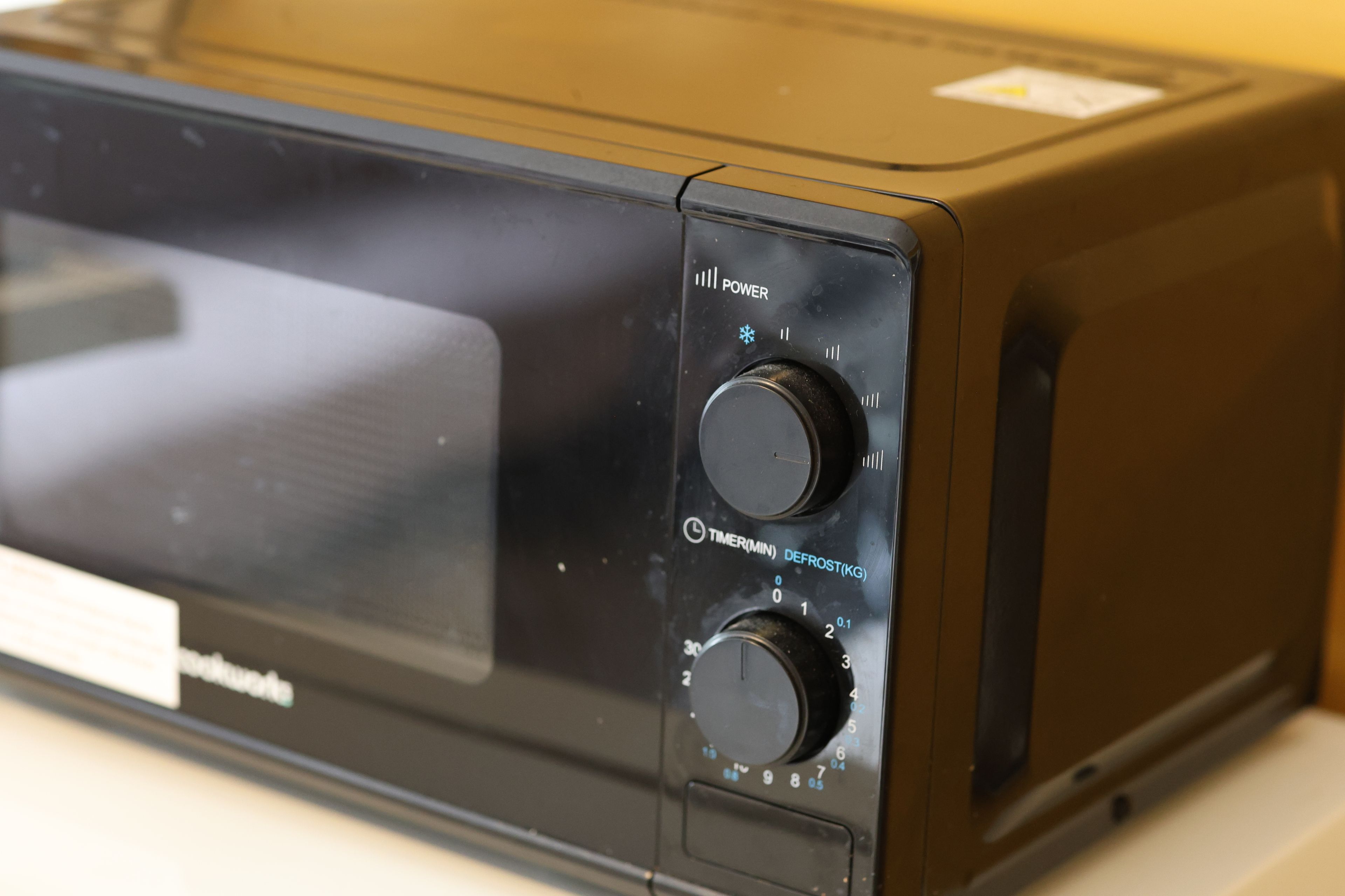 Een magnetron met twee draaiknoppen, waarvan één 'POWER' is aangeduid en de andere 'DEFROST(KG)'.