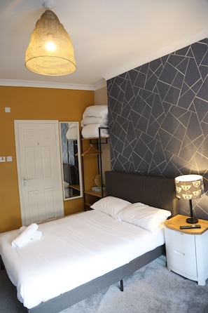 Een hotelkamer met een bed, nachtkastje, lamp, kledingkast en spiegel.