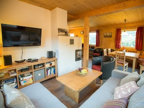 Uma sala de estar aconchegante com televisão de tela plana, estante de livros, mesa de centro com frutas e sofá com almofadas.