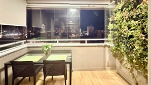 A modern balcony with a city view, a glass table with chairs, and a green wall with plants. - Vrbo Property (Sacramenta)