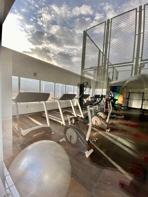 Une salle de sport équipée de matériel d’exercice, dotée d’une grande fenêtre et offrant une vue sur la ville.