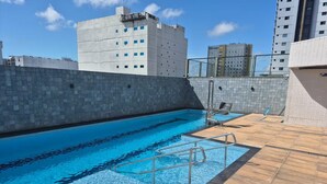 A rooftop swimming pool with clear blue water, surrounded by a tiled deck and a high-rise building in the background. - Vrbo Property (Sacramenta)