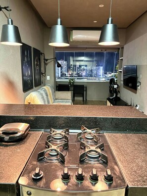 Une cuisine équipée d’une cuisinière à gaz, d’un éclairage au plafond et offrant une vue sur la ville par une fenêtre.