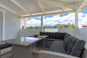 Ein überdachter Außenbereich mit Tischplatte aus Glas, gepolsterten Sofas und Blick auf die Landschaft.