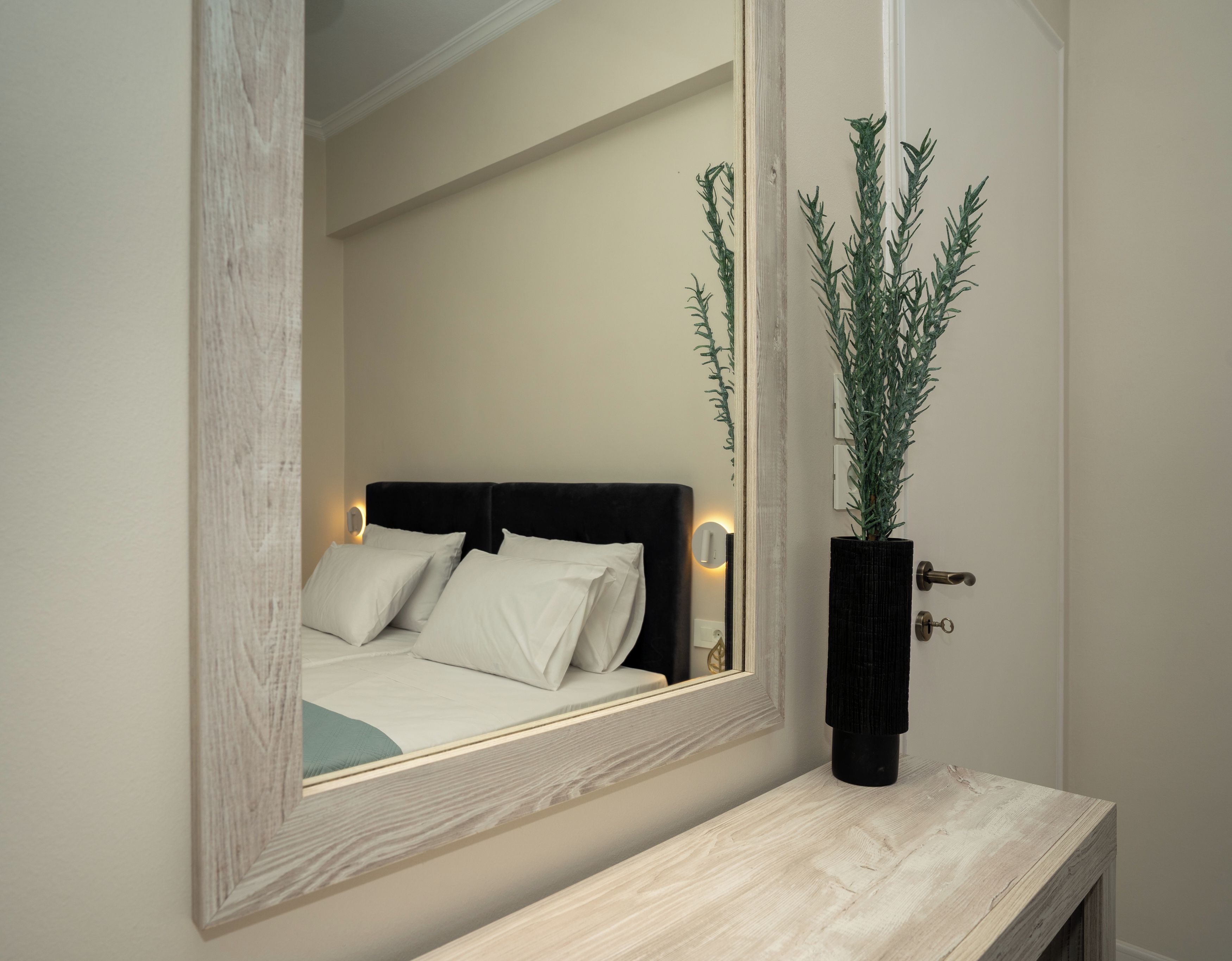 A bedroom with a bed, a bedside table, a mirror, and a potted plant.