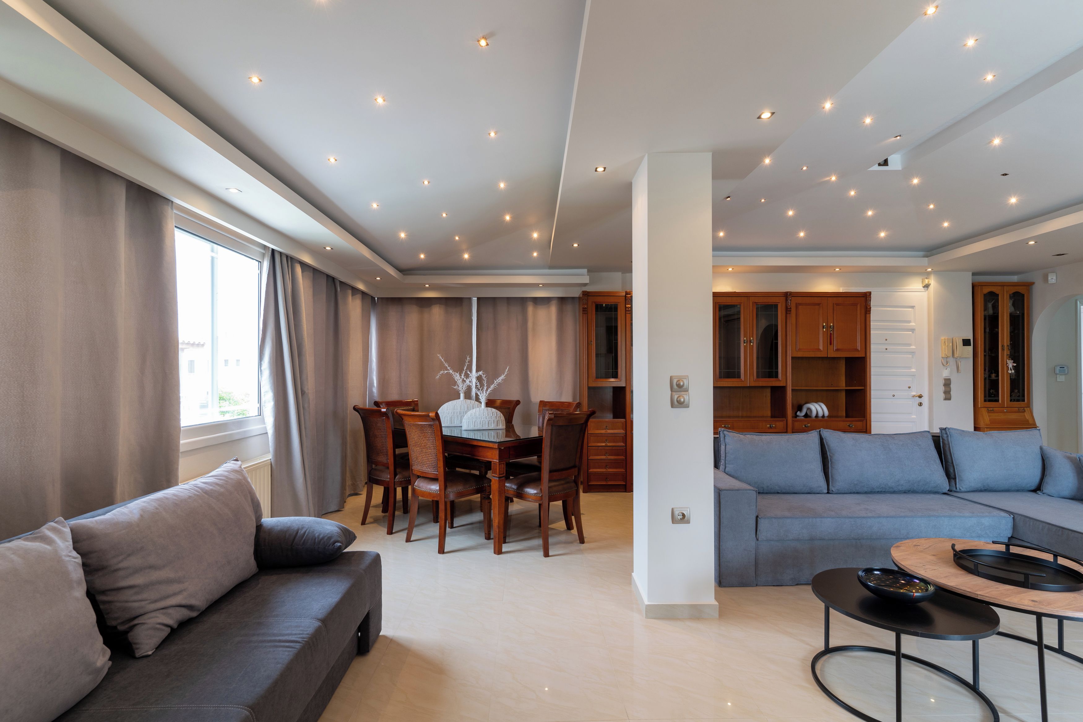 A modern living room with a sofa, a dining table with chairs, and a kitchen area with cabinets.