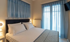 Ein Hotelzimmer mit einem Bett, Nachttischlampen, einer Heizung und durchsichtigen Vorhängen.