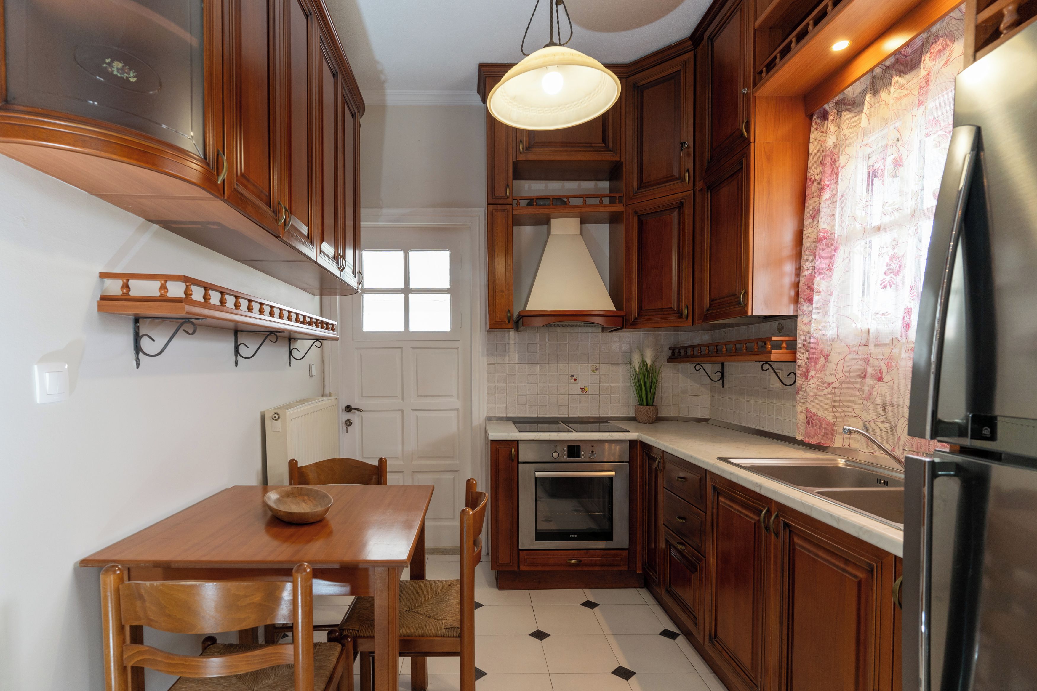 Cozinha com armários de madeira, mesa de jantar, cadeiras, luminária pendente, geladeira e painel de azulejos.