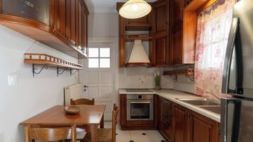 Cozinha com armários de madeira, mesa de jantar, cadeiras, luminária pendente, geladeira e painel de azulejos.