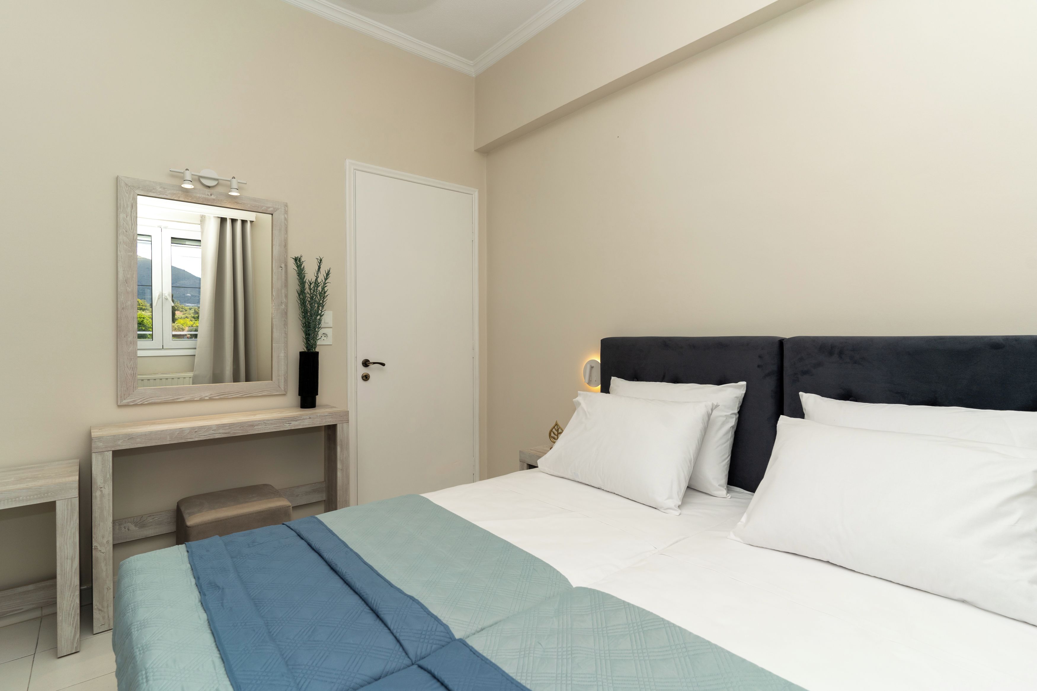 Quarto com cama, mesa de cabeceira, espelho e porta.