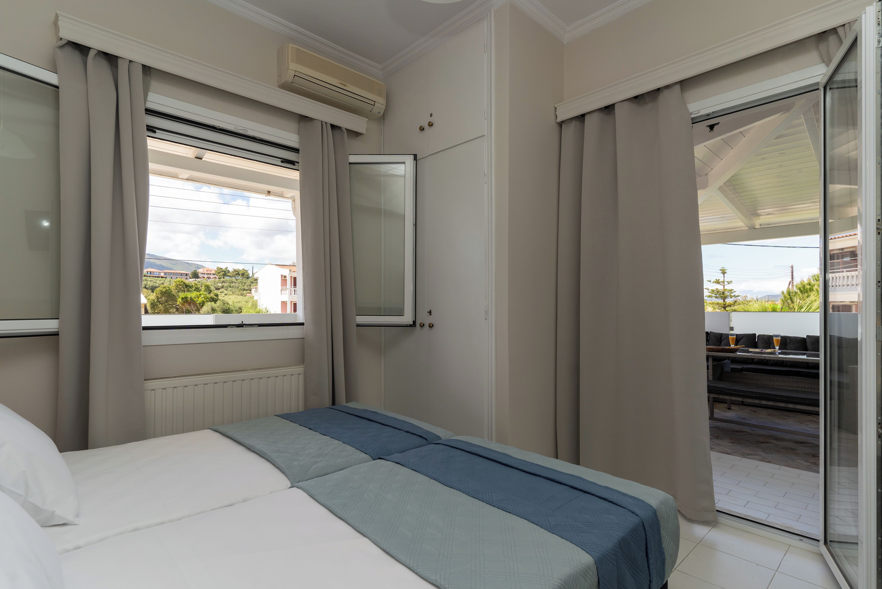 Quarto de hotel com cama, janela com cortinas, ar condicionado e vista para edifícios e áreas verdes.