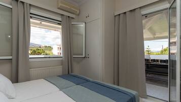 Quarto de hotel com cama, janela com cortinas, ar condicionado e vista para edifícios e áreas verdes.