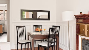 Uma sala de jantar com uma mesa posta para quatro pessoas, um espelho acima da mesa e uma lareira com uma luminária à direita.