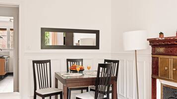A dining area with a table set for four, a mirror above the table, and a fireplace with a lamp to the right.