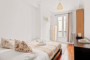 A bedroom with a bed, a bedside table, a lamp, and a window with curtains. - Elegant Apartment Near Eiffel Tower (Paris)